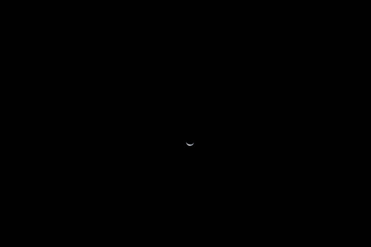 A crescent Earth seen from afar during the Artemis II mission, a delicate waning crescent suspended in the darkness of space.