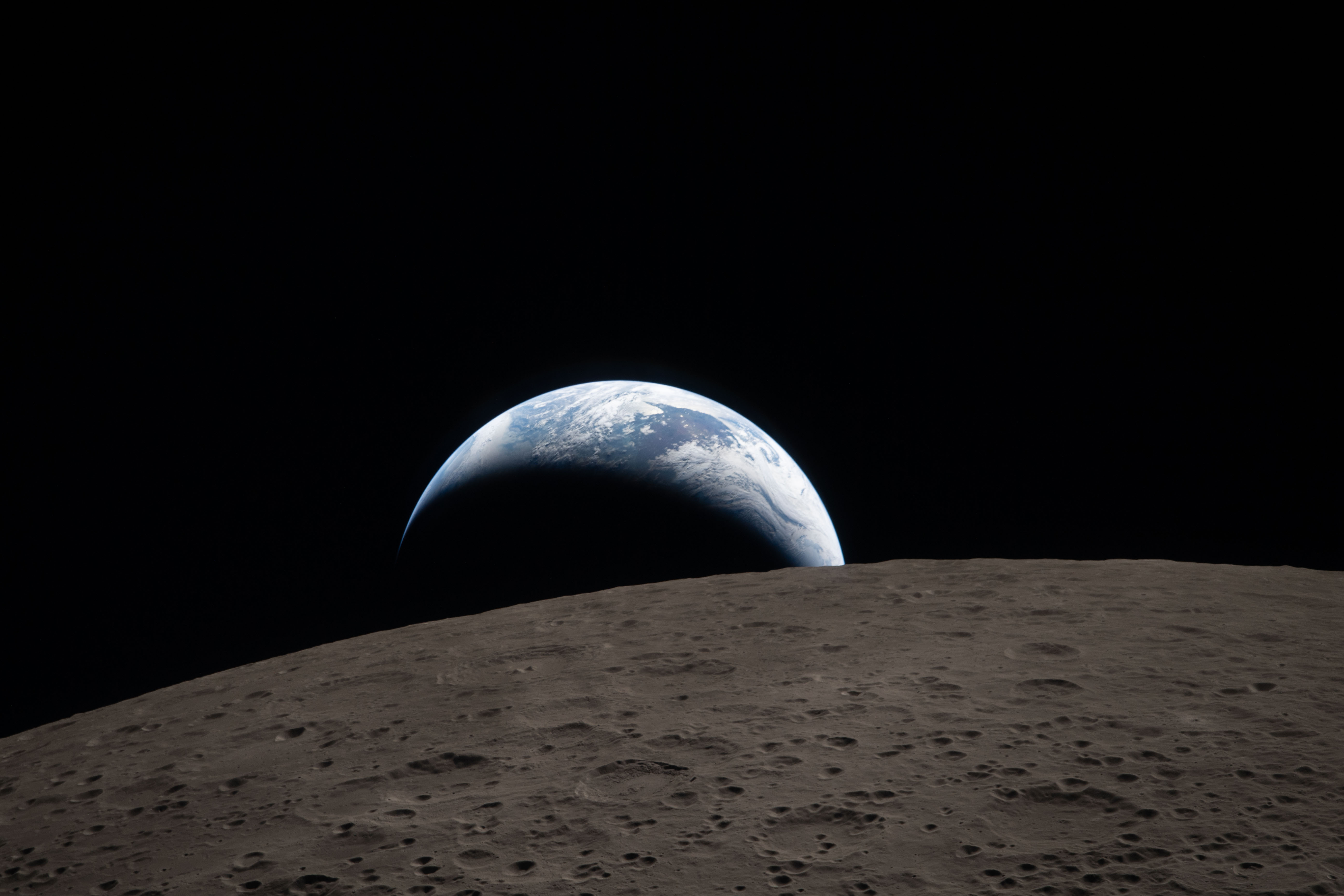 Earth setting behind the Moon's curved limb, captured from Orion during the Artemis II lunar flyby on April 6, 2026. Swirling clouds are visible over Australia and Oceania on Earth's day side.