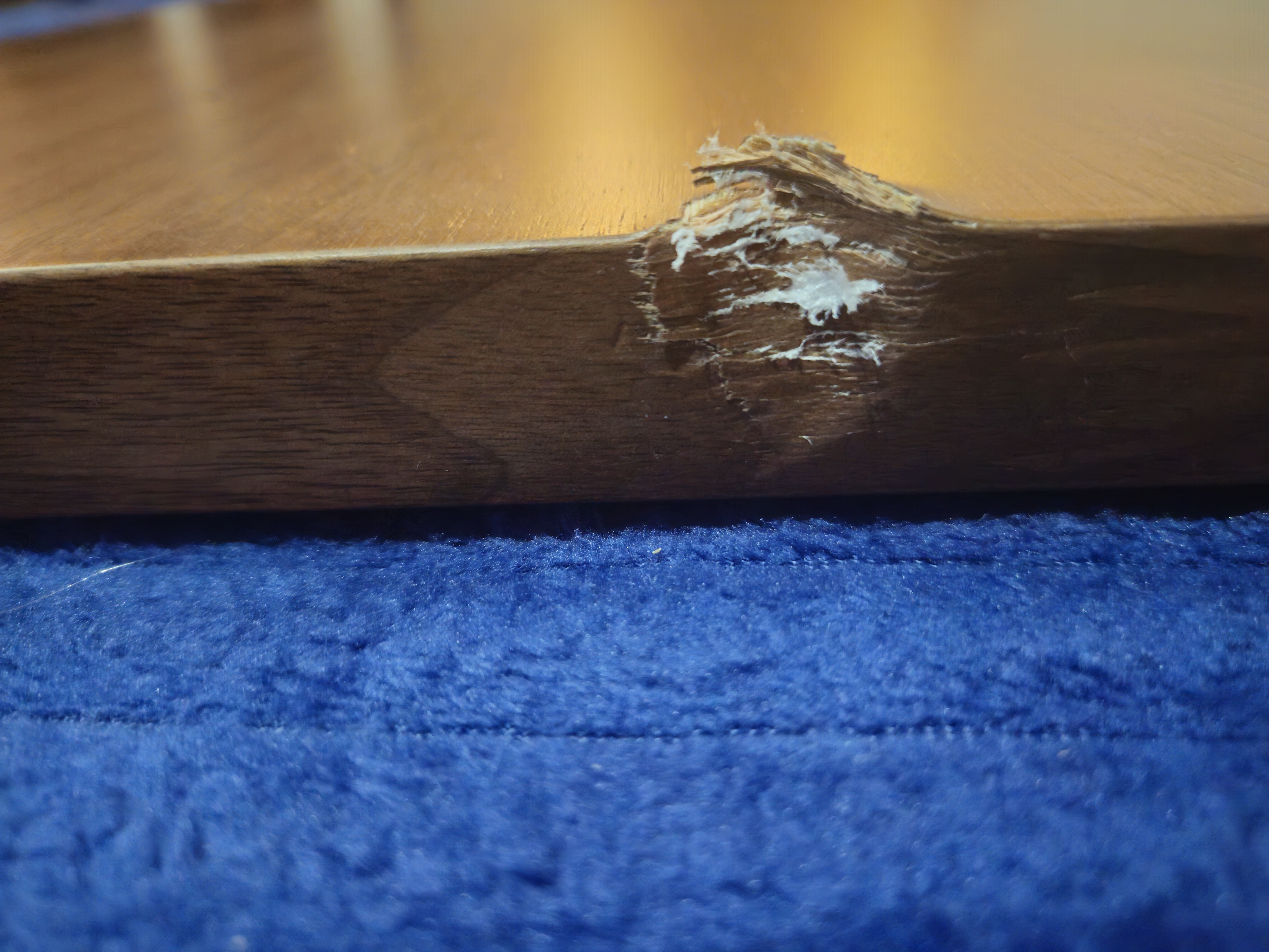 Close-up of damaged desktop edge showing quarter-sized gouge