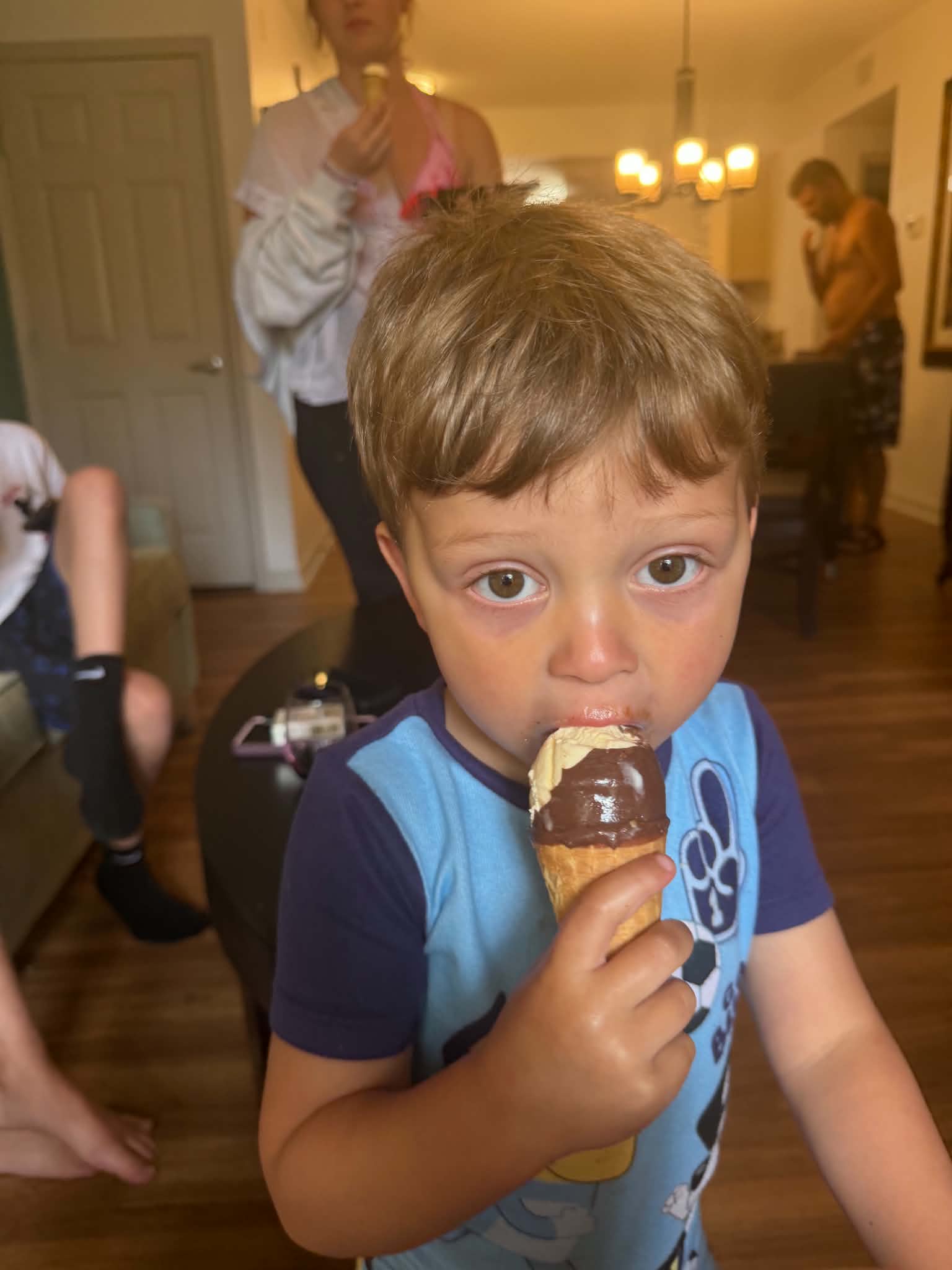 A young boy enjoying an ice cream cone in the resort room with family members in the background