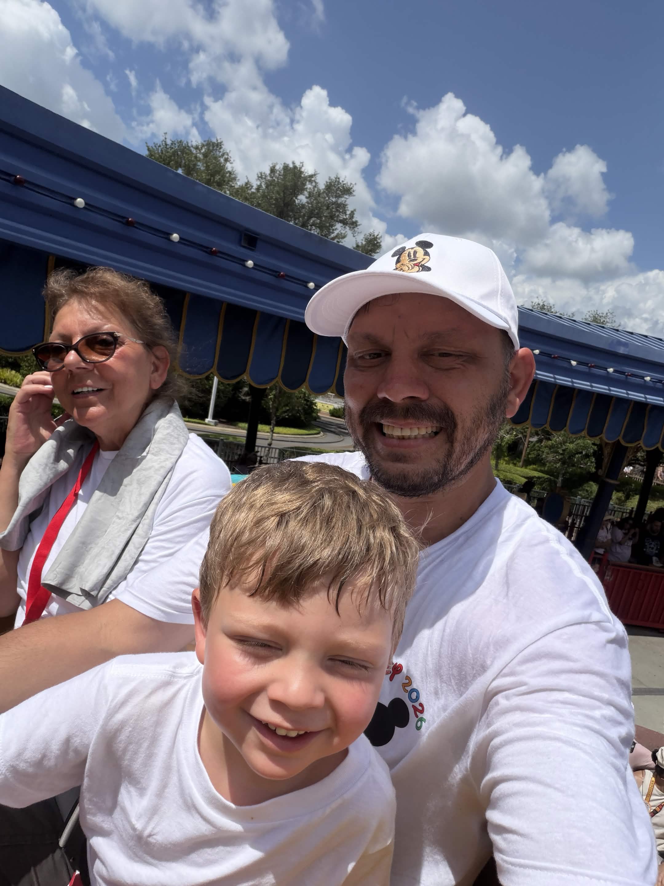 Family selfie near Dumbo and Storybook Circus with blue canopy and sunny sky