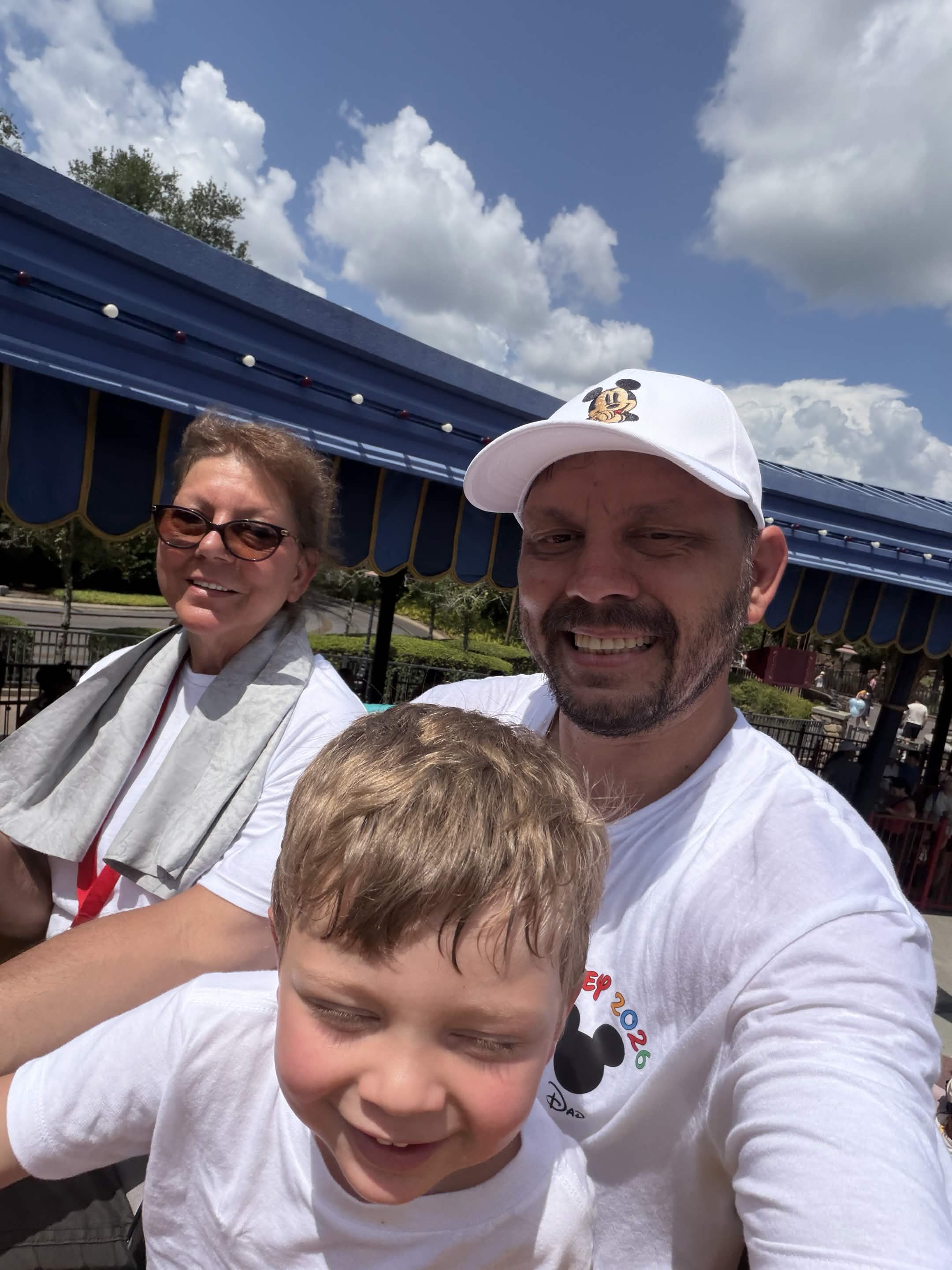 Family selfie in matching Disney shirts under the blue canopy at Storybook Circus