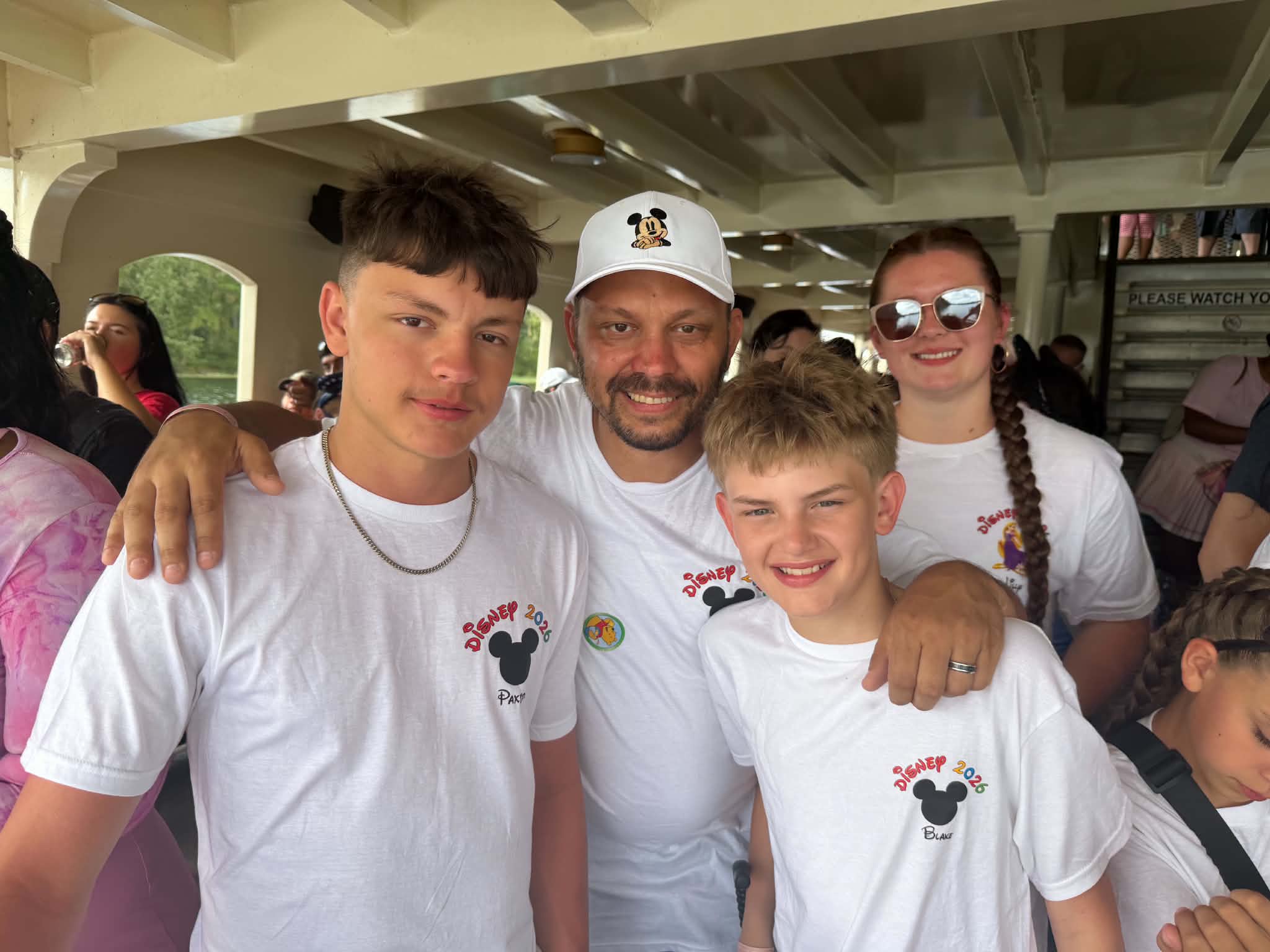 Family smiling on the ferry in matching Disney 2026 shirts