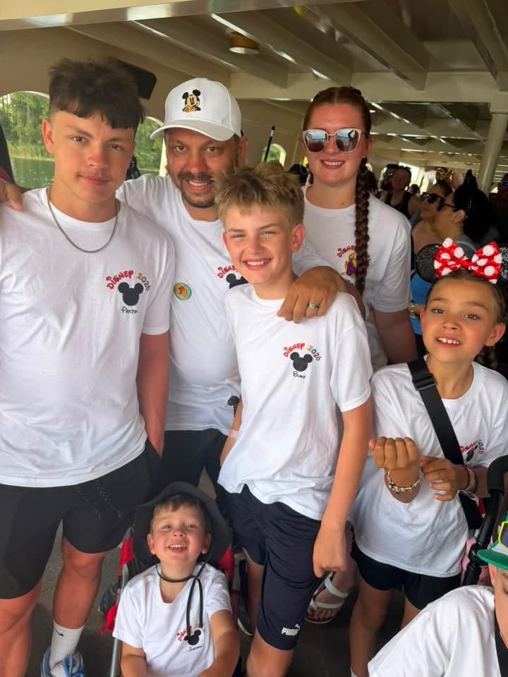 Close-up group photo of family members in matching white Disney shirts standing on a covered ferry deck