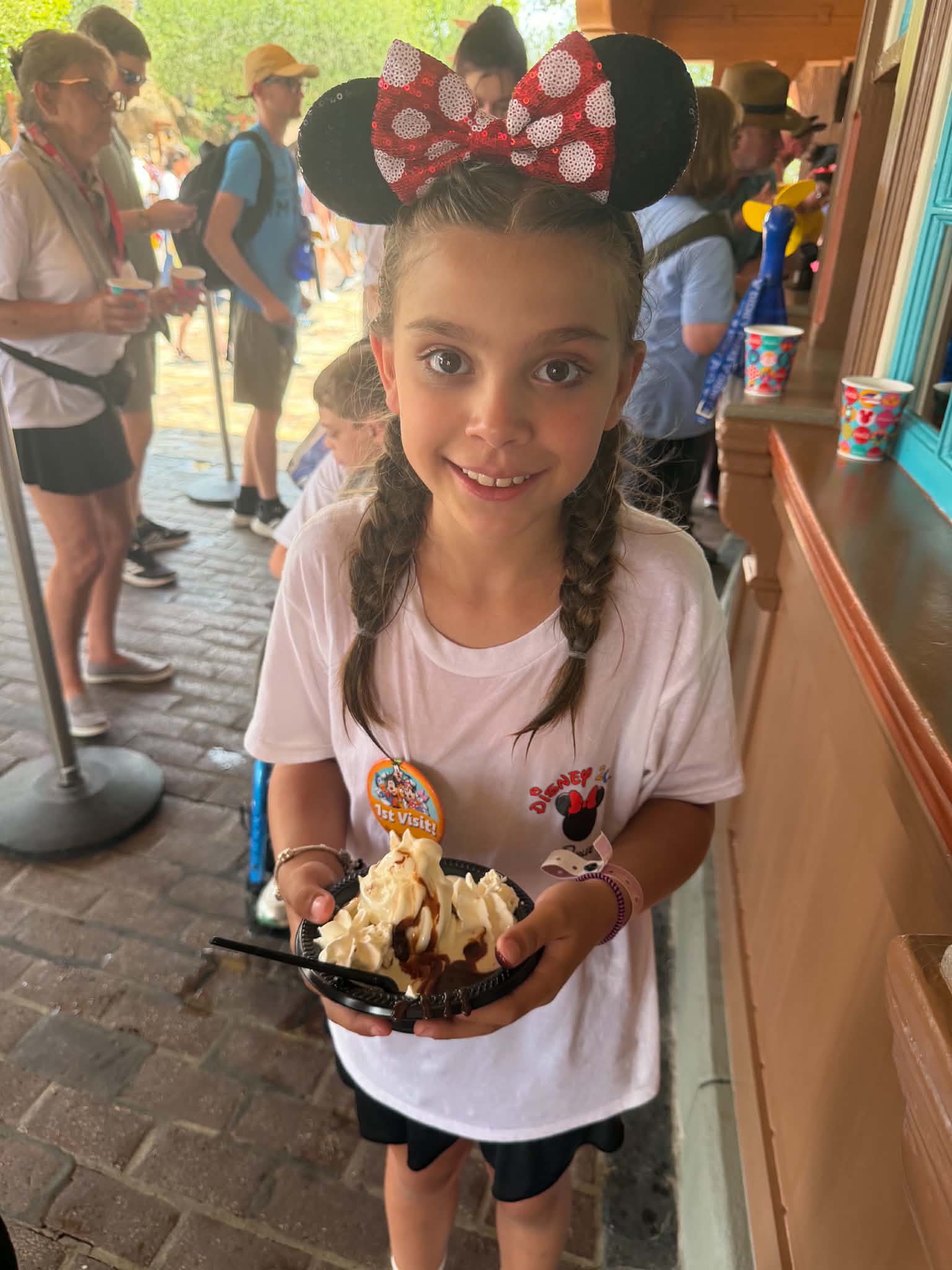 Young girl with Minnie ears and a first-visit button holding an ice cream sundae