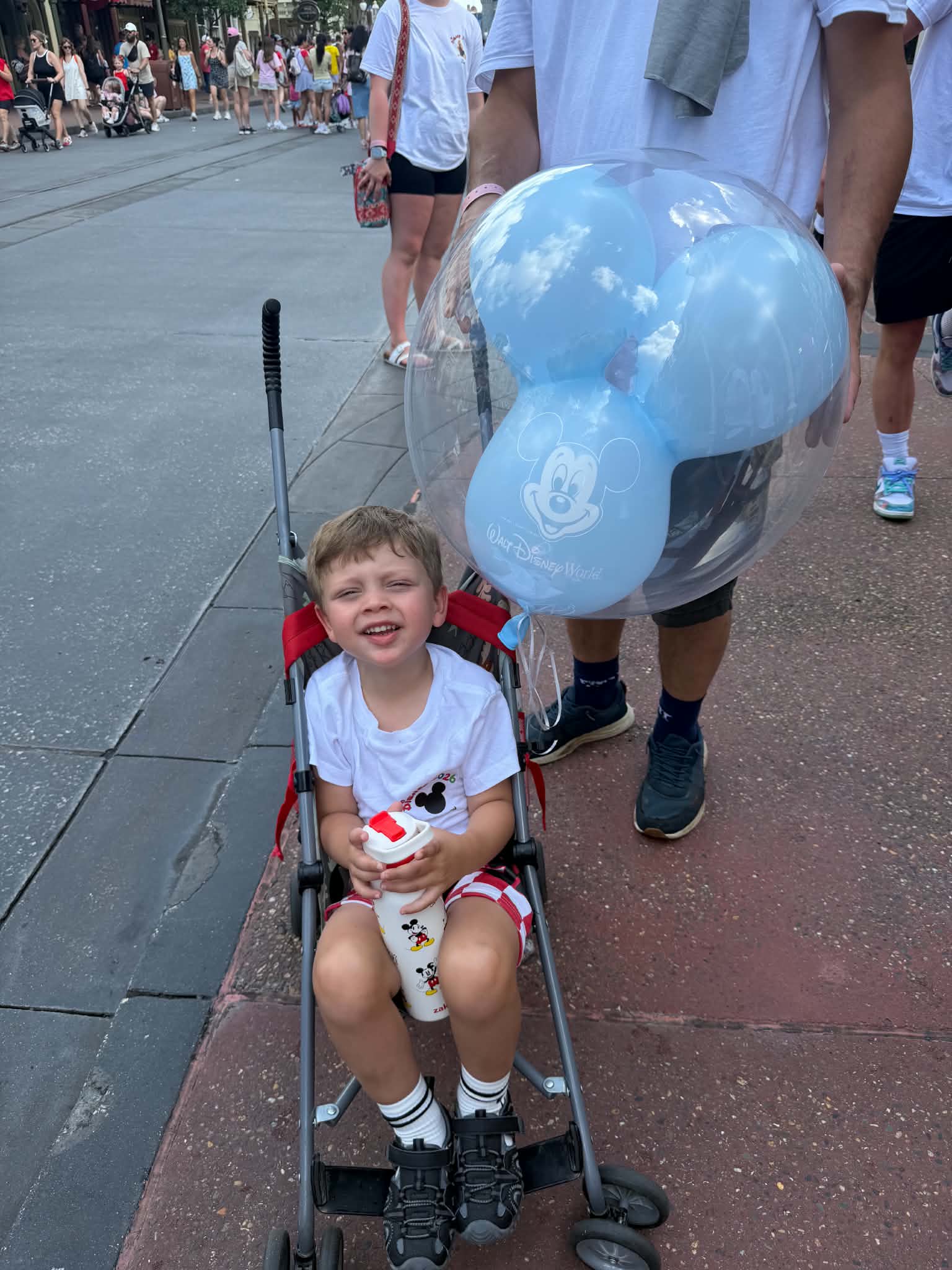 Young boy smiling in a stroller with a blue Walt Disney World Mickey balloon