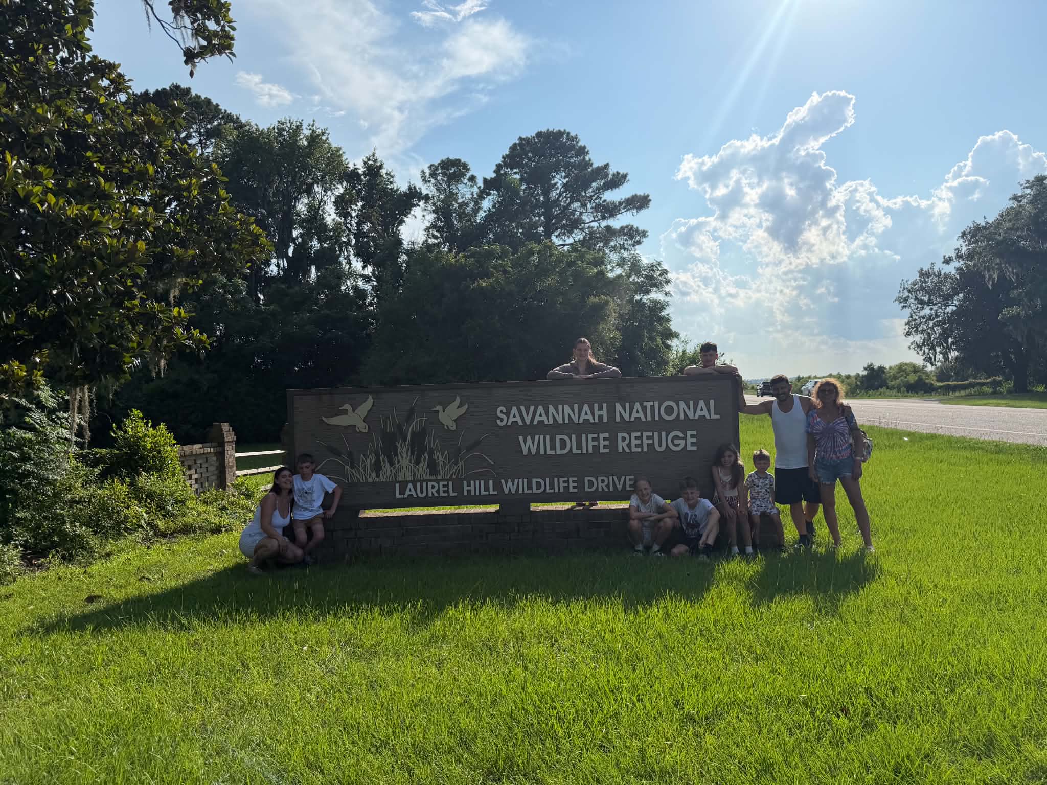 Wide backlit group photo at the refuge sign under dramatic clouds